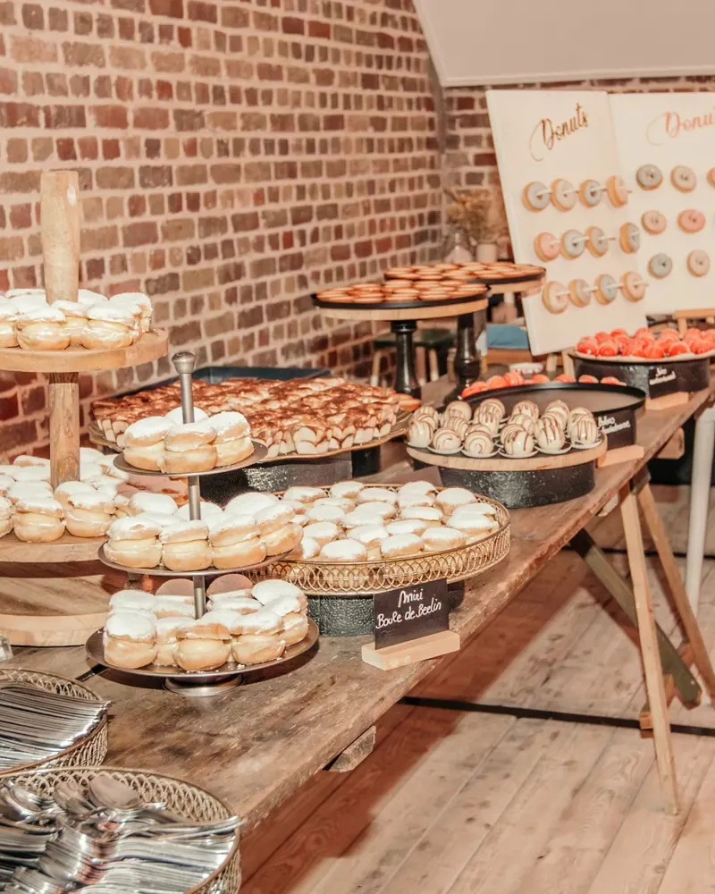 Dessertbuffet met etagères vol gebakjes en een donutwand tegen een bakstenen muur
