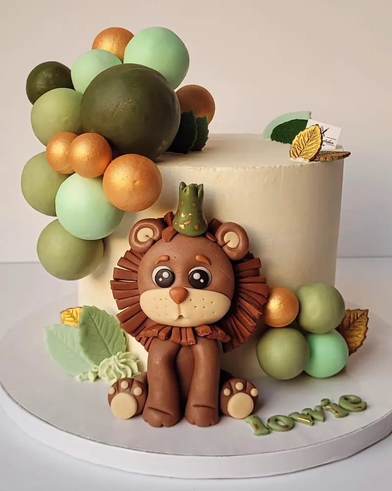 Witte taart met een leeuwtje van suikerpasta en groene, gouden en beige suikerballen