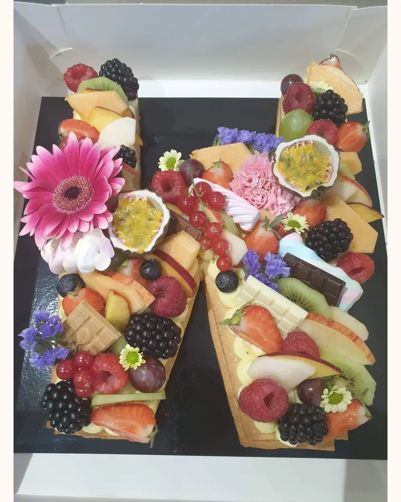Lettertaart in de vorm van een M met vers fruit en eetbare bloemen