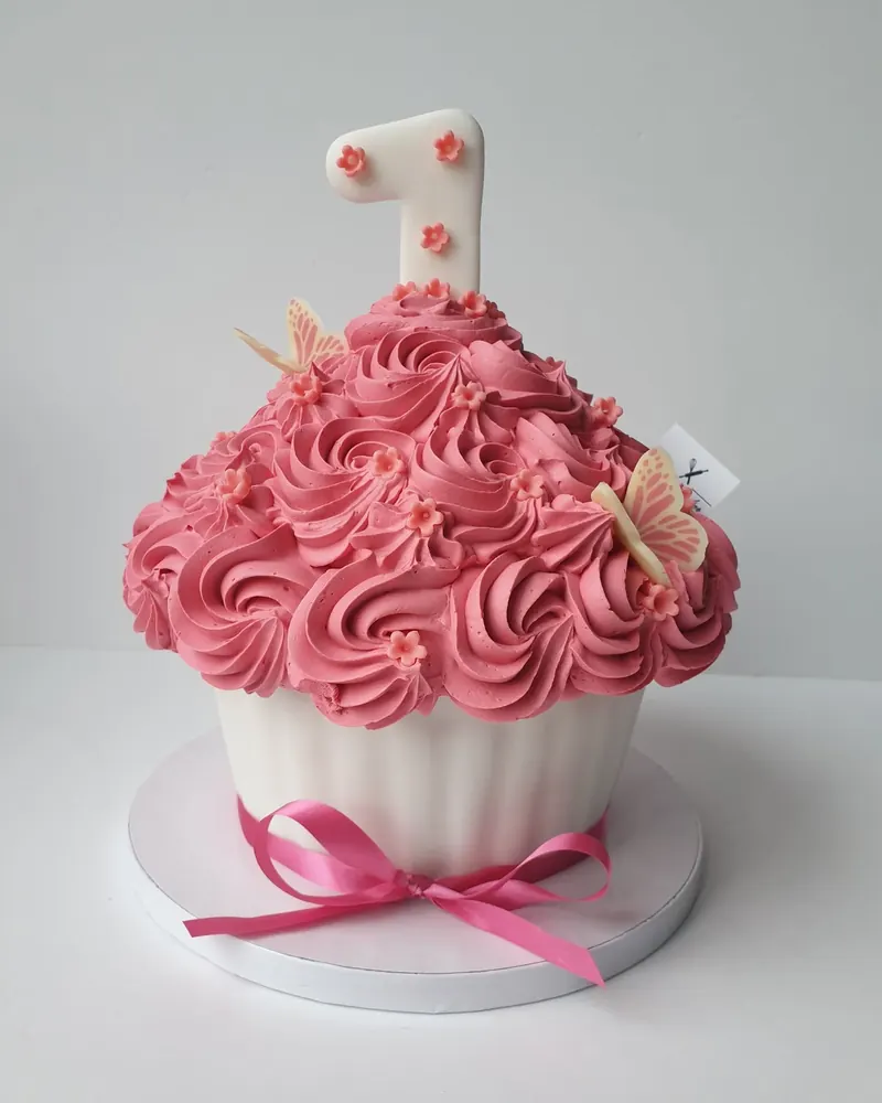Reuzecupcake-taart met roze botercrème-rozetten, een roze strik en een cijfer 1 erbovenop